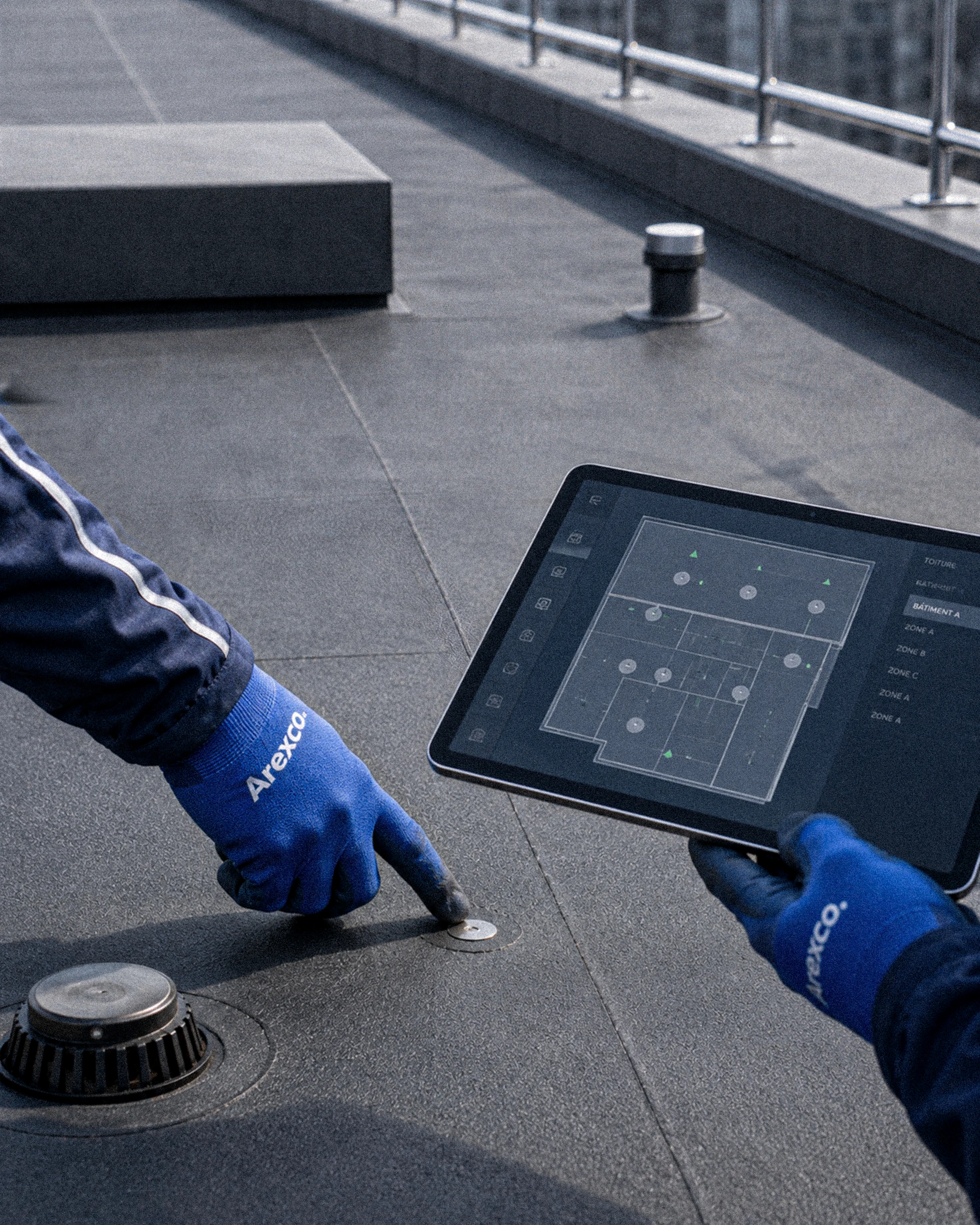 Technicien utilisant une tablette de cartographie pour piloter la gestion d'une toiture-terrasse moderne.