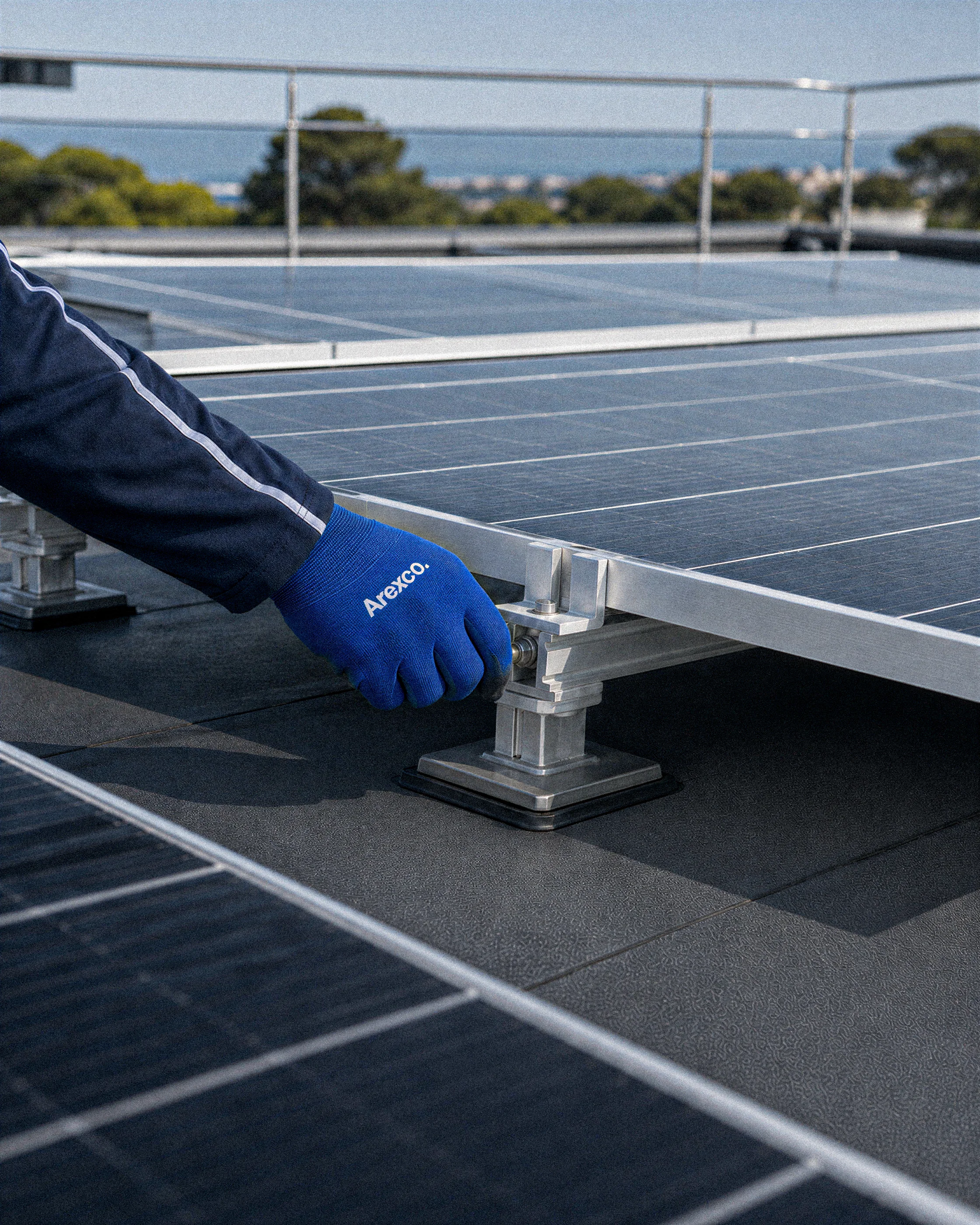 Main gantée ajustant une fixation de panneau photovoltaïque sur une toiture-terrasse moderne.
